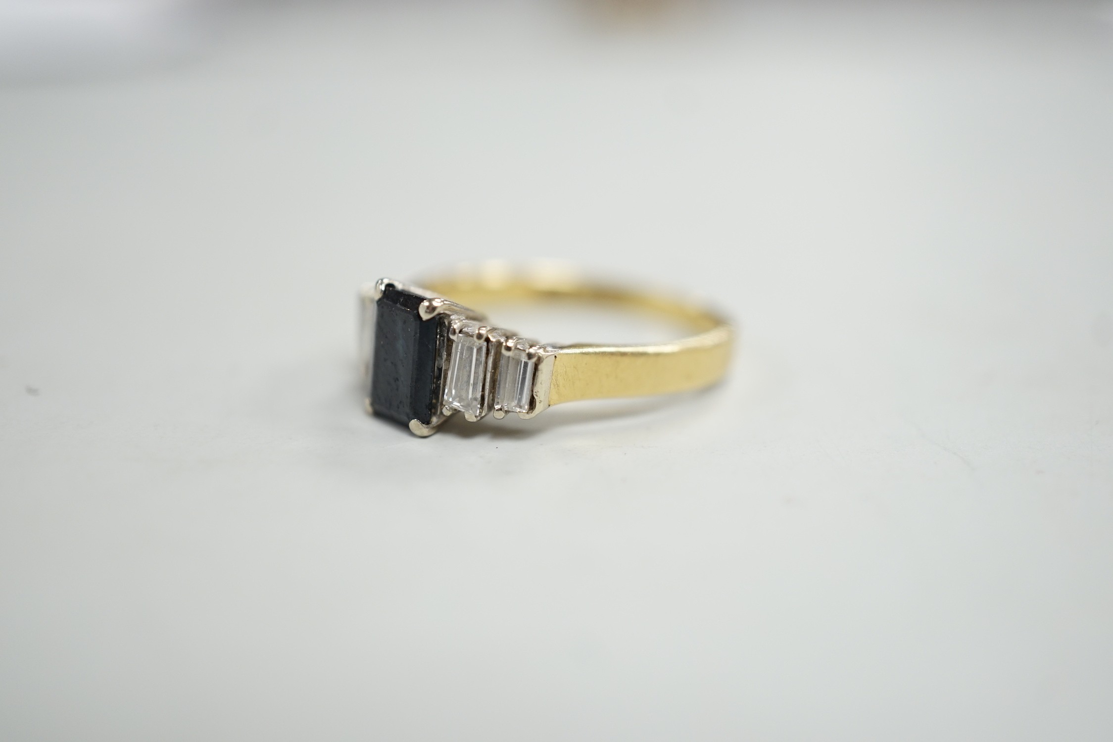 A modern 18ct gold and single stone emerald cut sapphire set ring, with graduated baguette cut diamond set shoulders, size J/K, gross weight 3.1 grams.